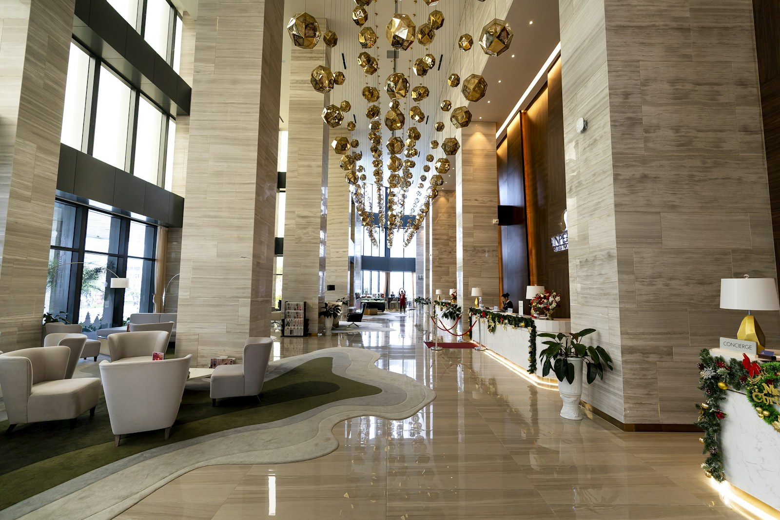 Modern hotel lobby with double-height ceiling, gold pendant cluster, and polished stone floor