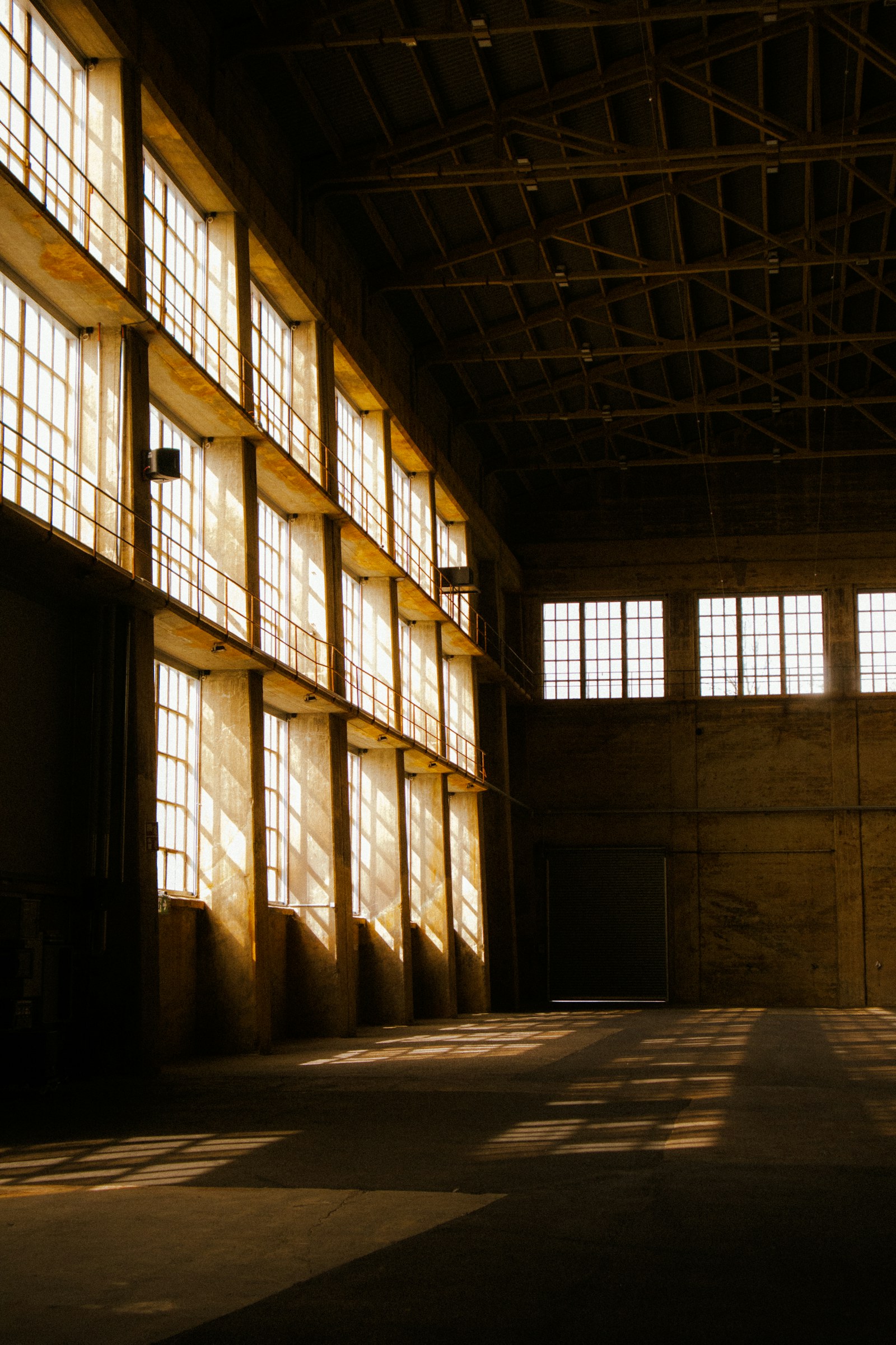 Warm afternoon light streams through tall warehouse windows, casting long shadows across the empty floor